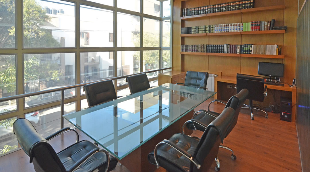 Sala de reuniones del estudio con mesa de vidrio y biblioteca jurídica
